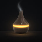 LUMUNO Aroma Diffuser in Walnut with cool mist rising and a warm amber glow